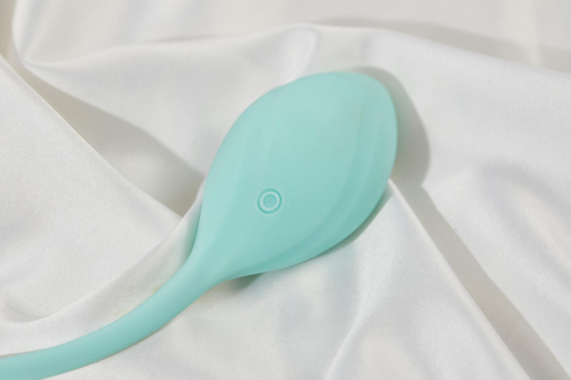A stylish teal vibrator on smooth white silk fabric, perfect for intimate recovery.