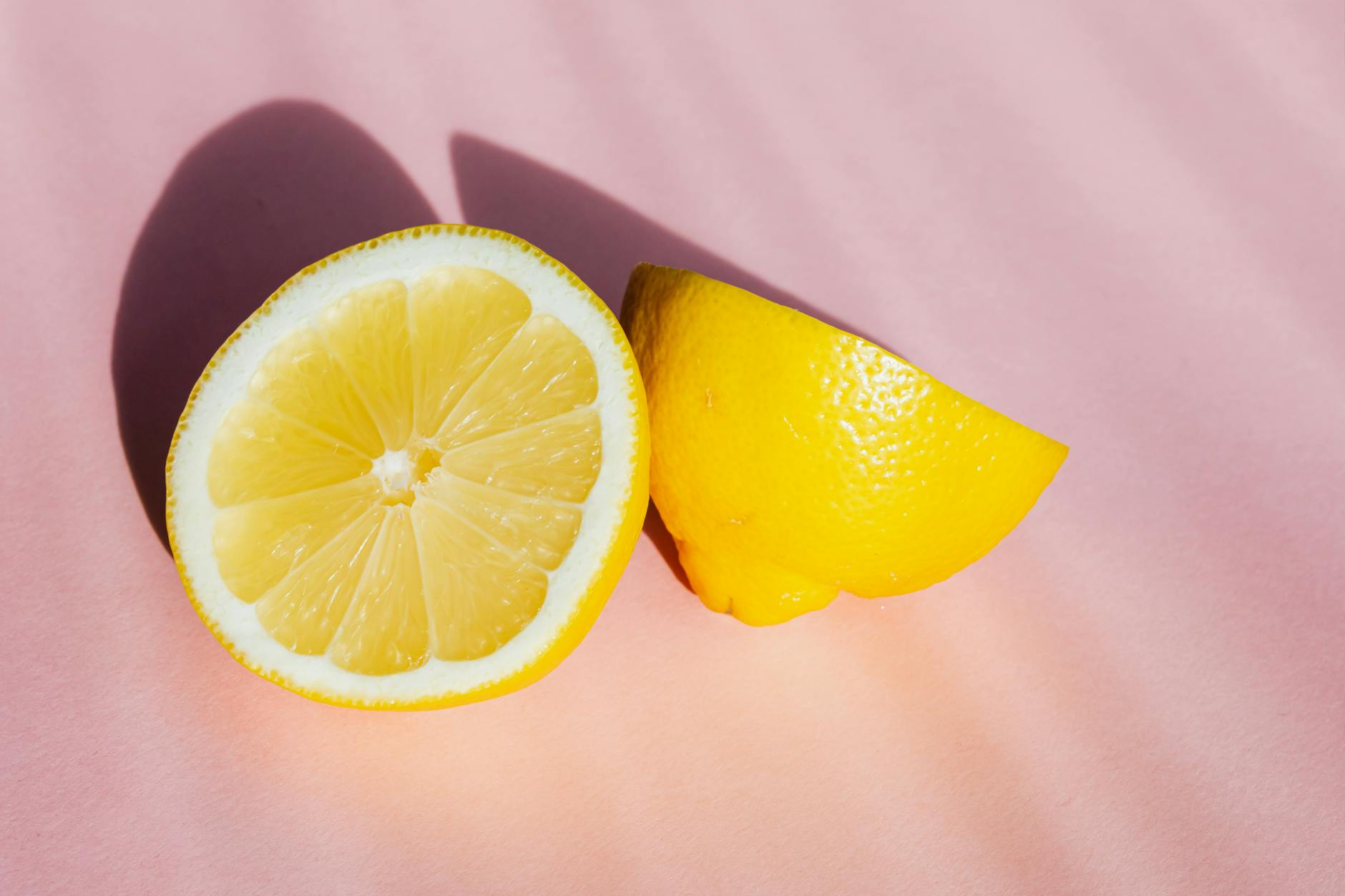 Fresh lemons in bright sunlight on a pink background, symbolizing the slow build of warmth