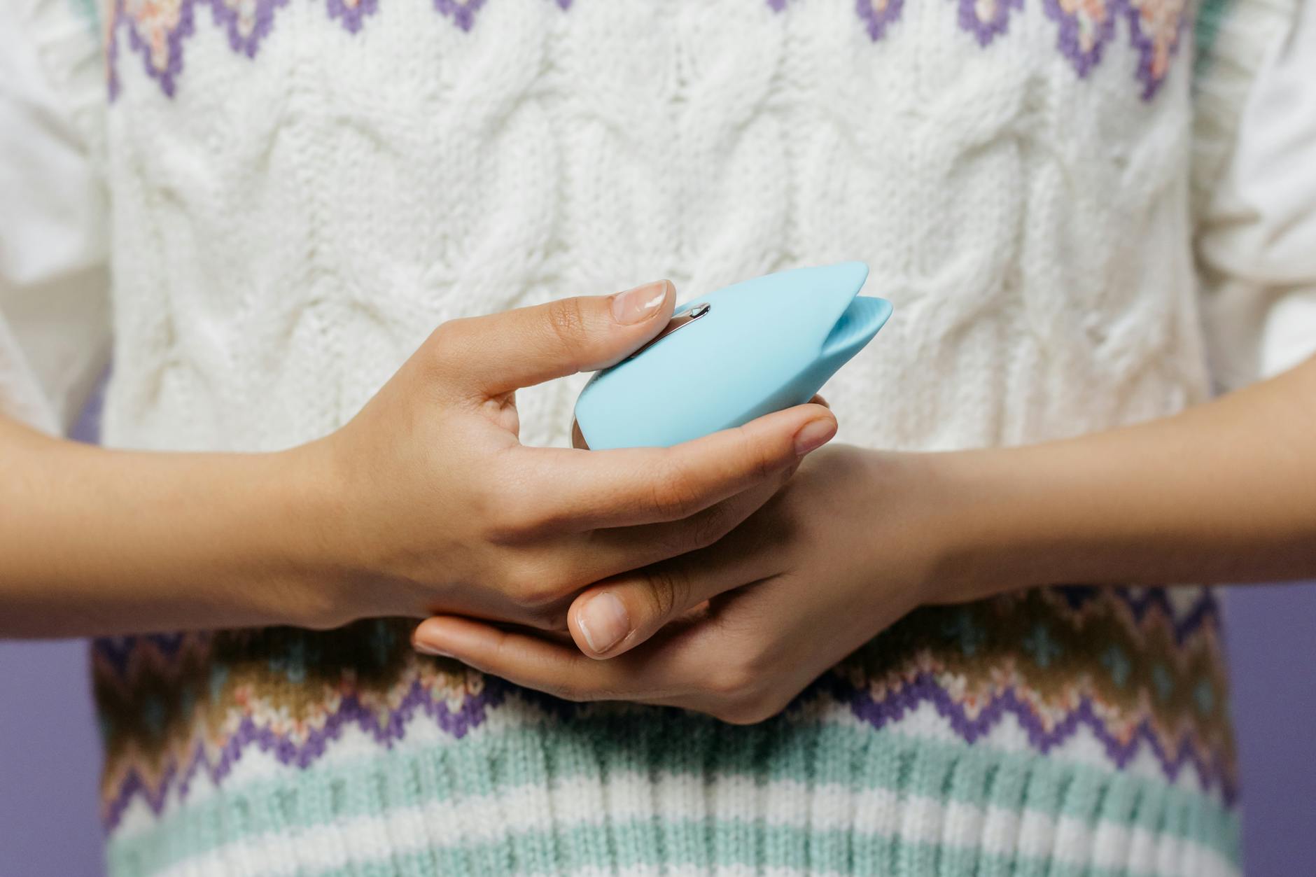 Close-up of hands holding a blue personal massager against a knitted sweater, showing gentle touch and control.